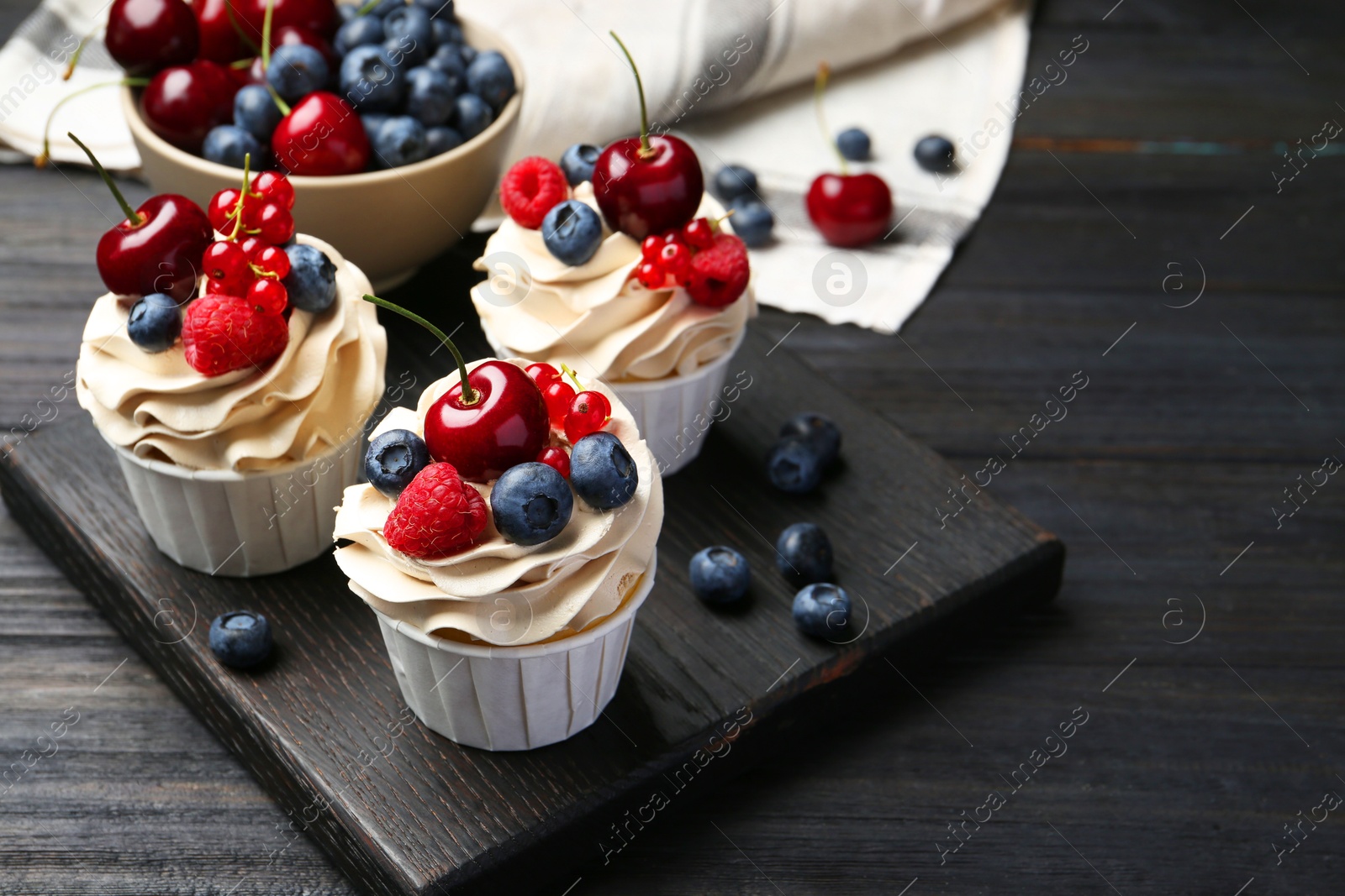 Photo of Tasty cupcakes with different berries on black wooden table, space for text