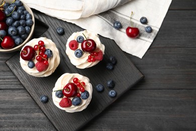 Photo of Tasty cupcakes with different berries on black wooden table, flat lay. Space for text