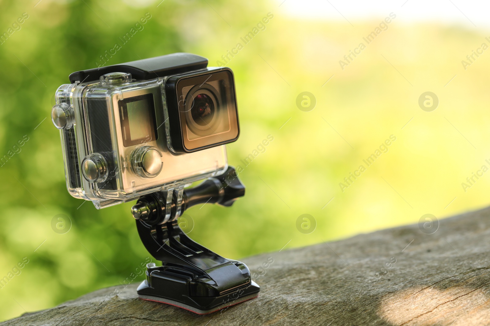 Photo of Modern action camera with mount on wooden surface outdoors, closeup. Space for text