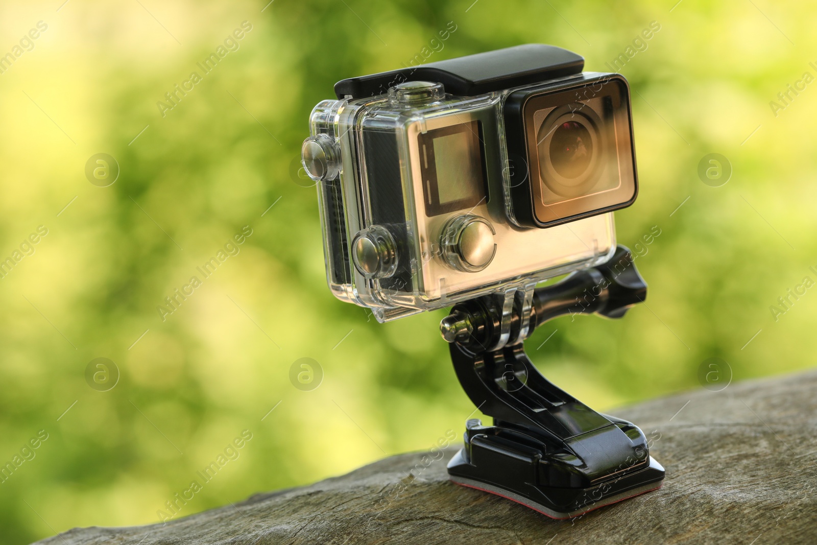 Photo of Modern action camera with mount on wooden surface outdoors, closeup