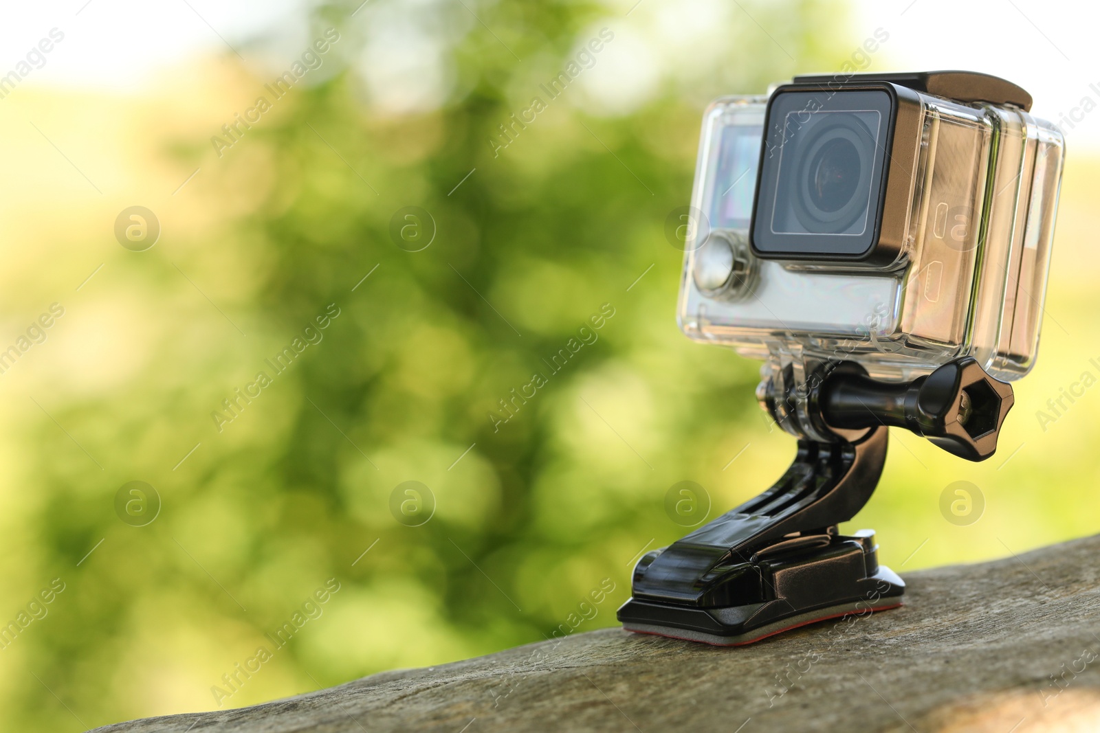 Photo of Modern action camera with mount on wooden surface outdoors, closeup. Space for text