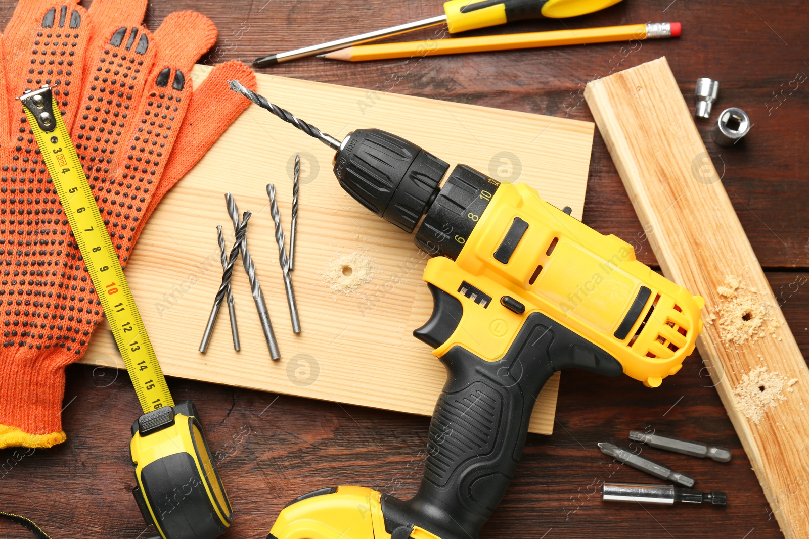 Photo of Cordless electric drill, gloves, pencil and construction tools on wooden table, flat lay