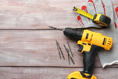 Photo of Cordless electric drill, gloves, bits and measuring tape on wooden table, flat lay. Space for text