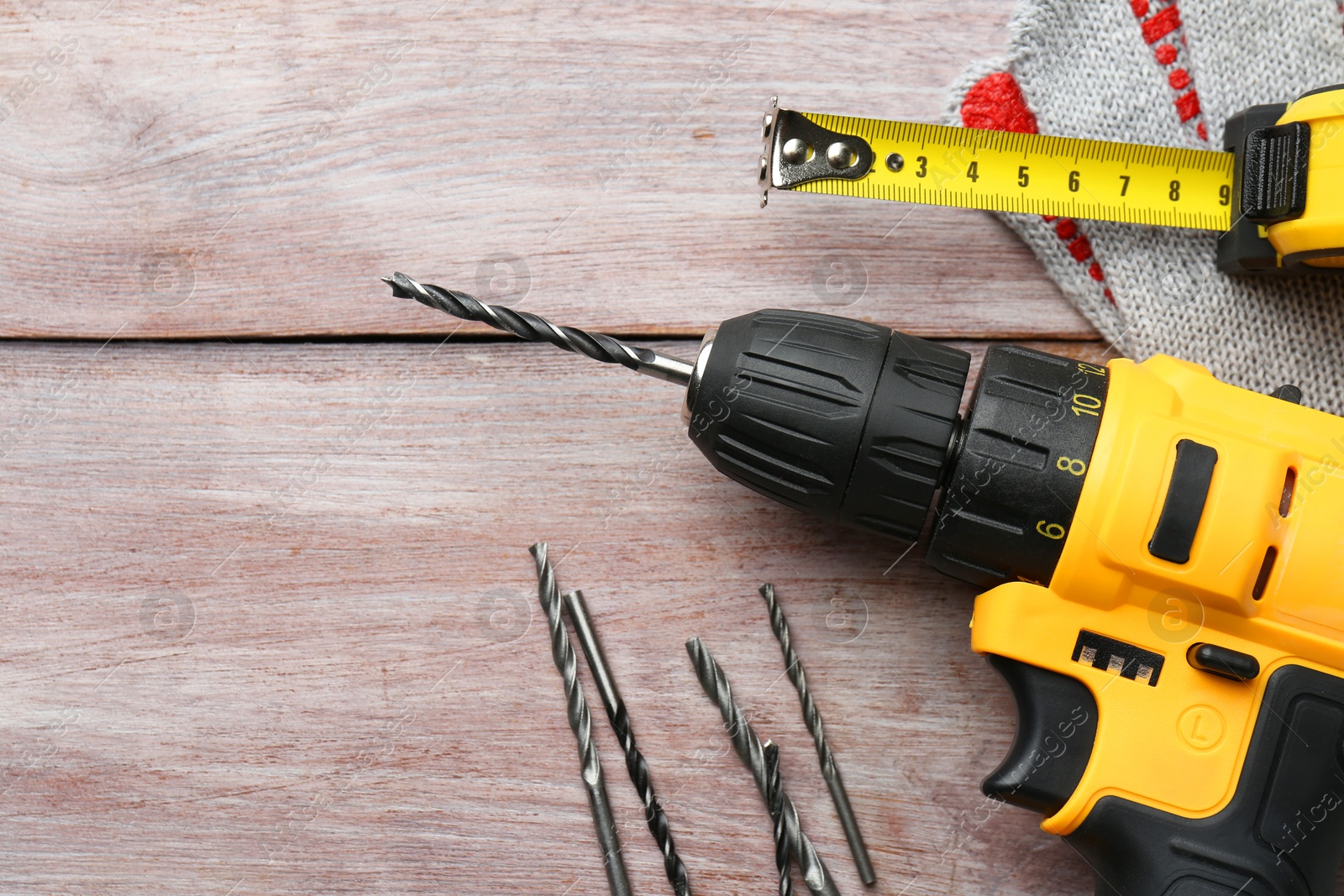 Photo of Cordless electric drill, bits and measuring tape on wooden table, flat lay. Space for text