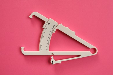 Photo of Plastic body fat caliper on pink background, top view