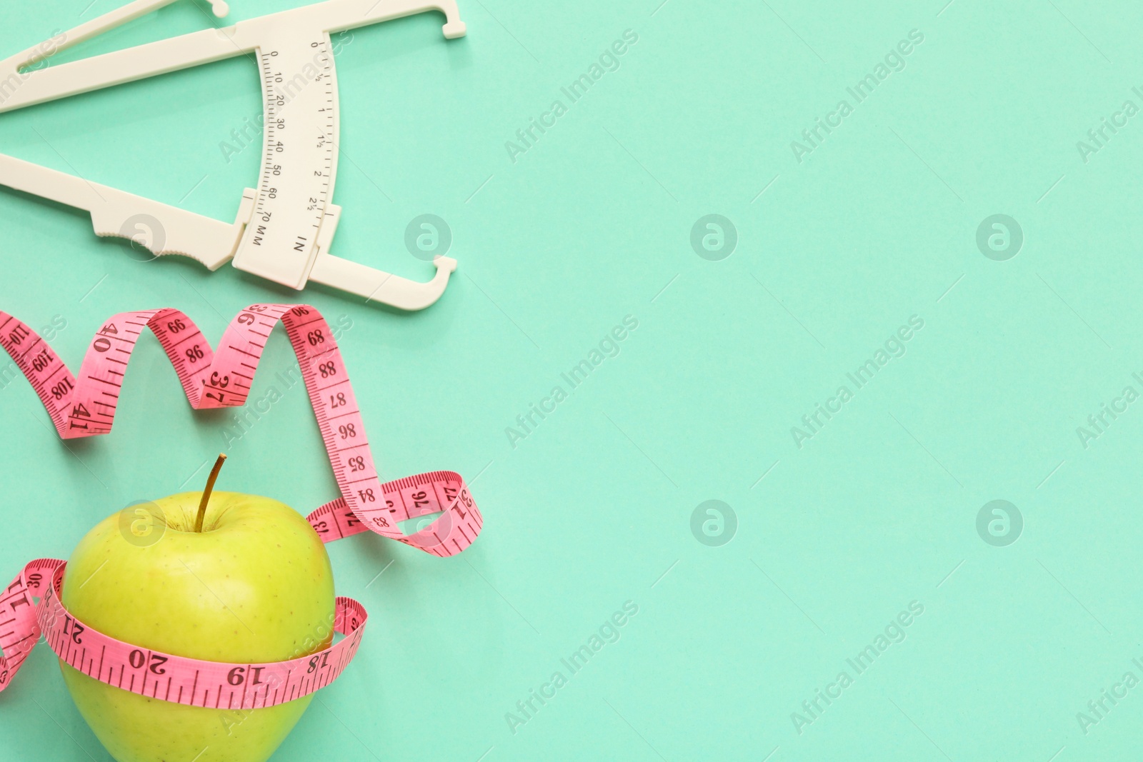 Photo of Body fat caliper, measuring tape and apple on turquoise background, flat lay. Space for text