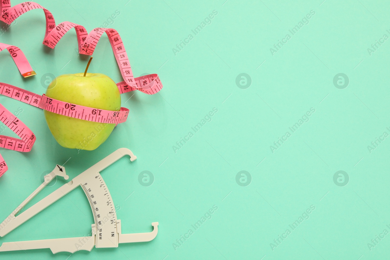 Photo of Body fat caliper, measuring tape and apple on turquoise background, flat lay. Space for text