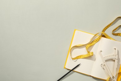 Photo of Body fat caliper, measuring tape and notebook on grey background, flat lay. Space for text