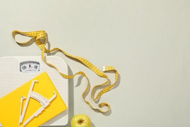 Photo of Body fat caliper, measuring tape, scale and notebook on light grey background, flat lay. Space for text