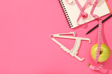 Photo of Body fat caliper, measuring tape, notebook and apple on pink background, flat lay. Space for text