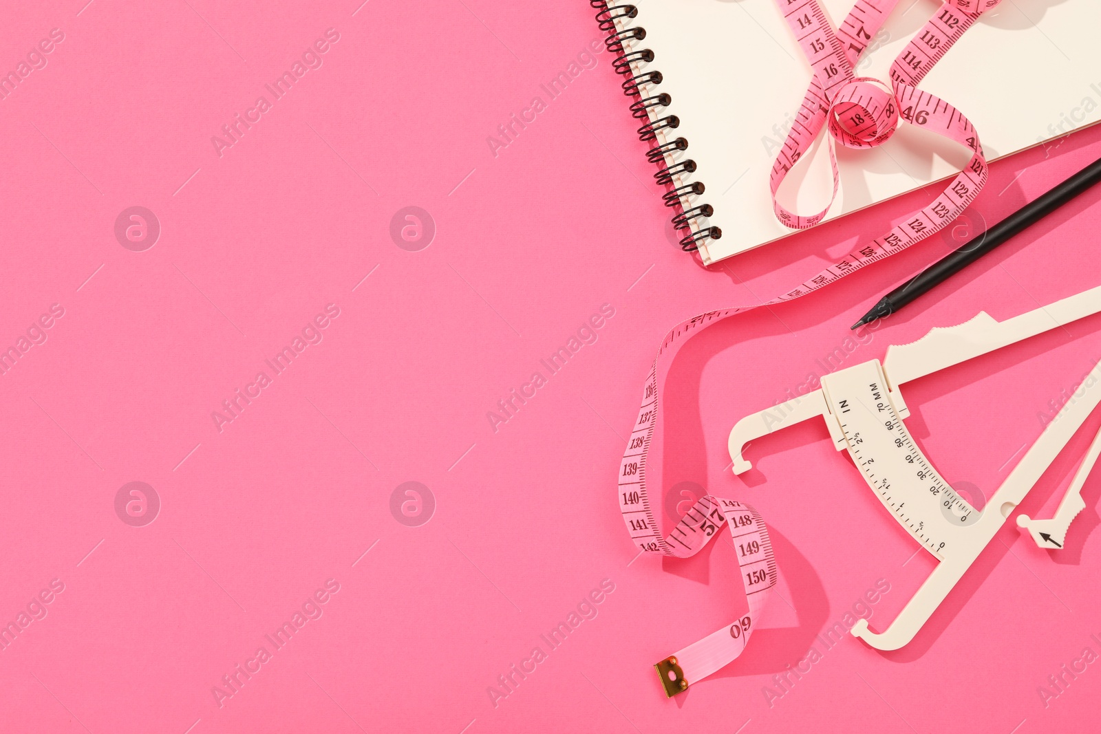 Photo of Body fat caliper, measuring tape, notebook and pencil on pink background, flat lay. Space for text