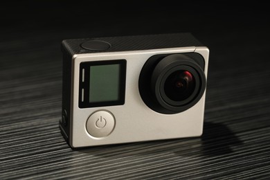 Modern action camera on wooden table against black background, closeup