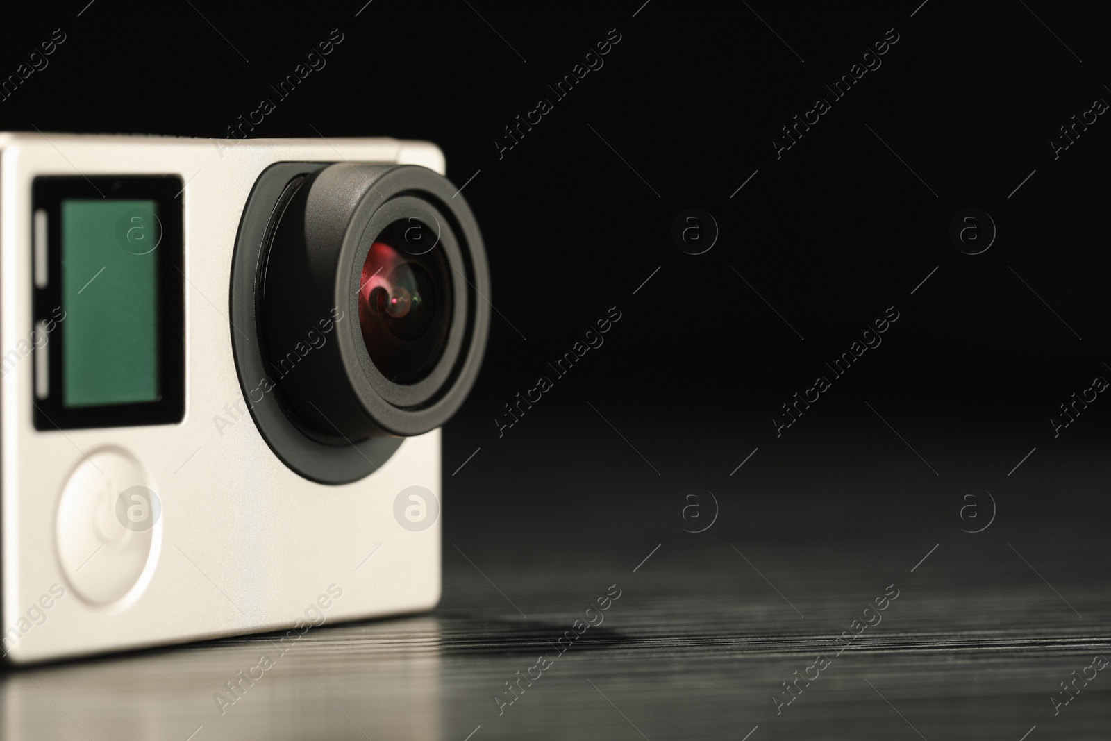 Photo of Modern action camera on wooden table against black background, closeup. Space for text