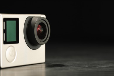 Photo of Modern action camera on wooden table against black background, closeup. Space for text