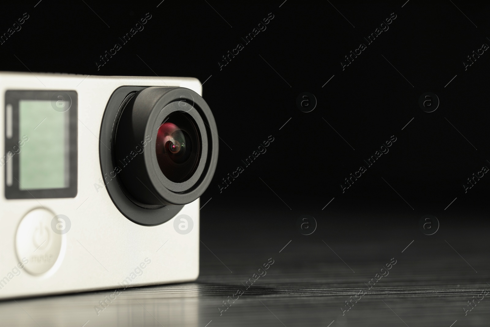 Photo of Modern action camera on wooden table against black background, closeup. Space for text