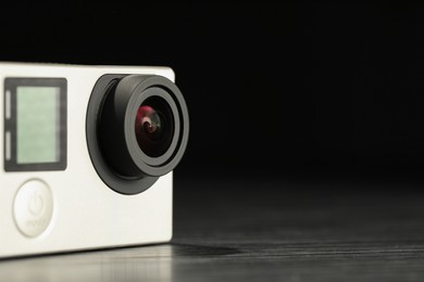 Photo of Modern action camera on wooden table against black background, closeup. Space for text