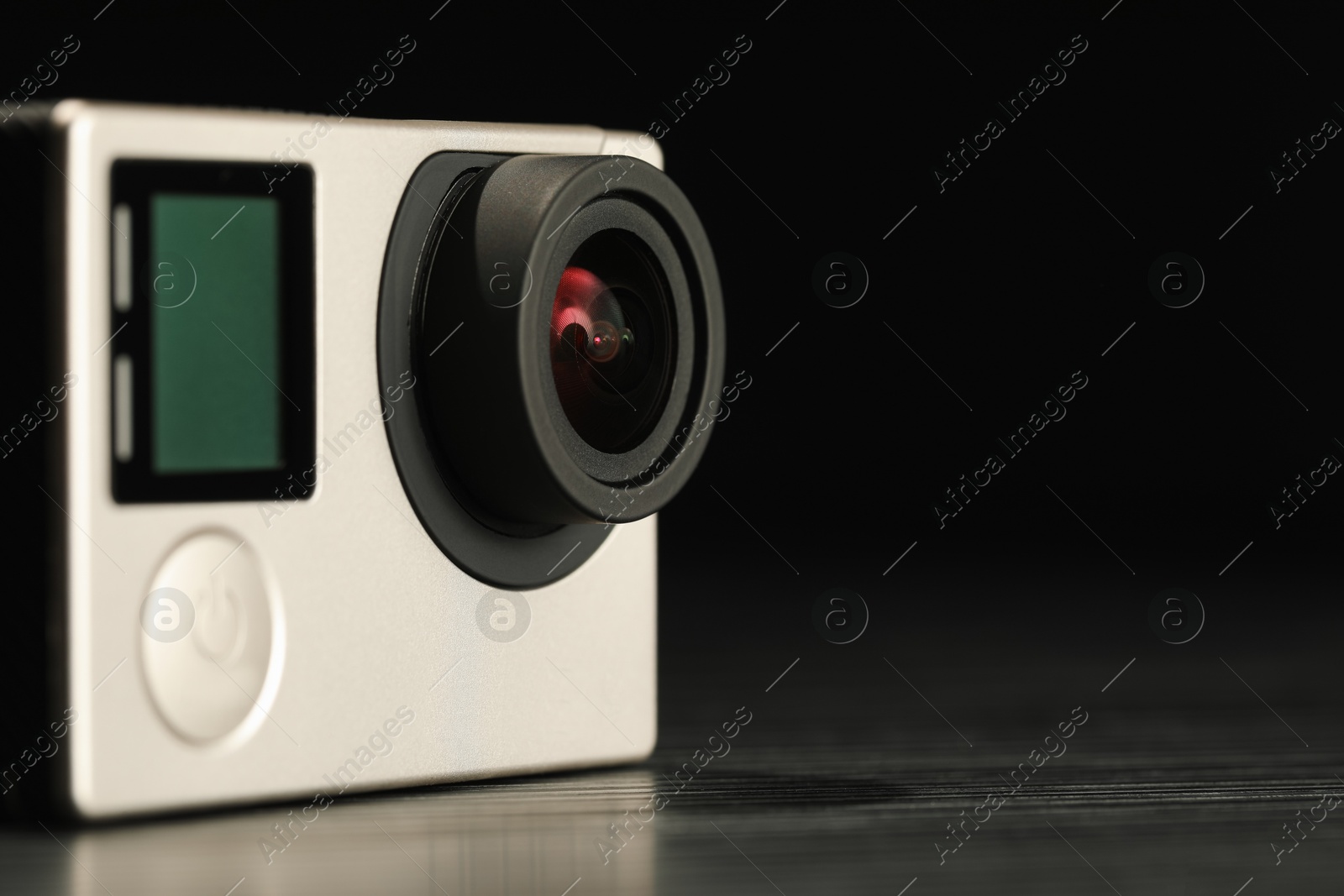 Photo of Modern action camera on wooden table against black background, closeup. Space for text