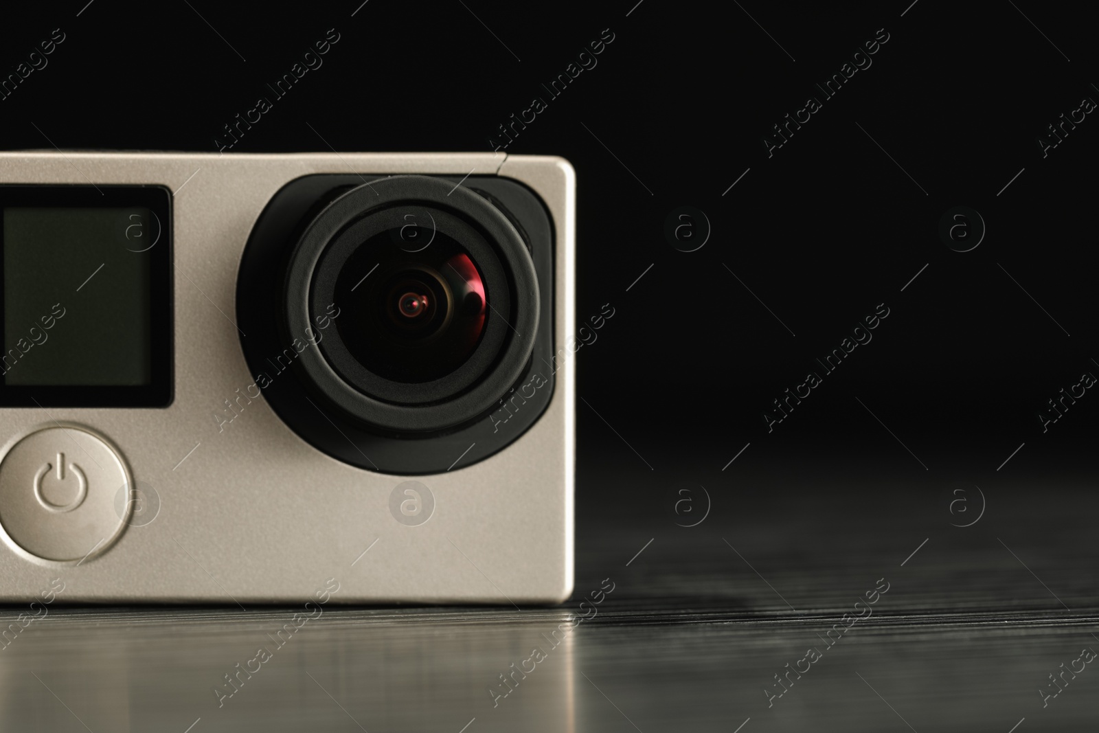 Photo of Modern action camera on wooden table against black background, closeup. Space for text