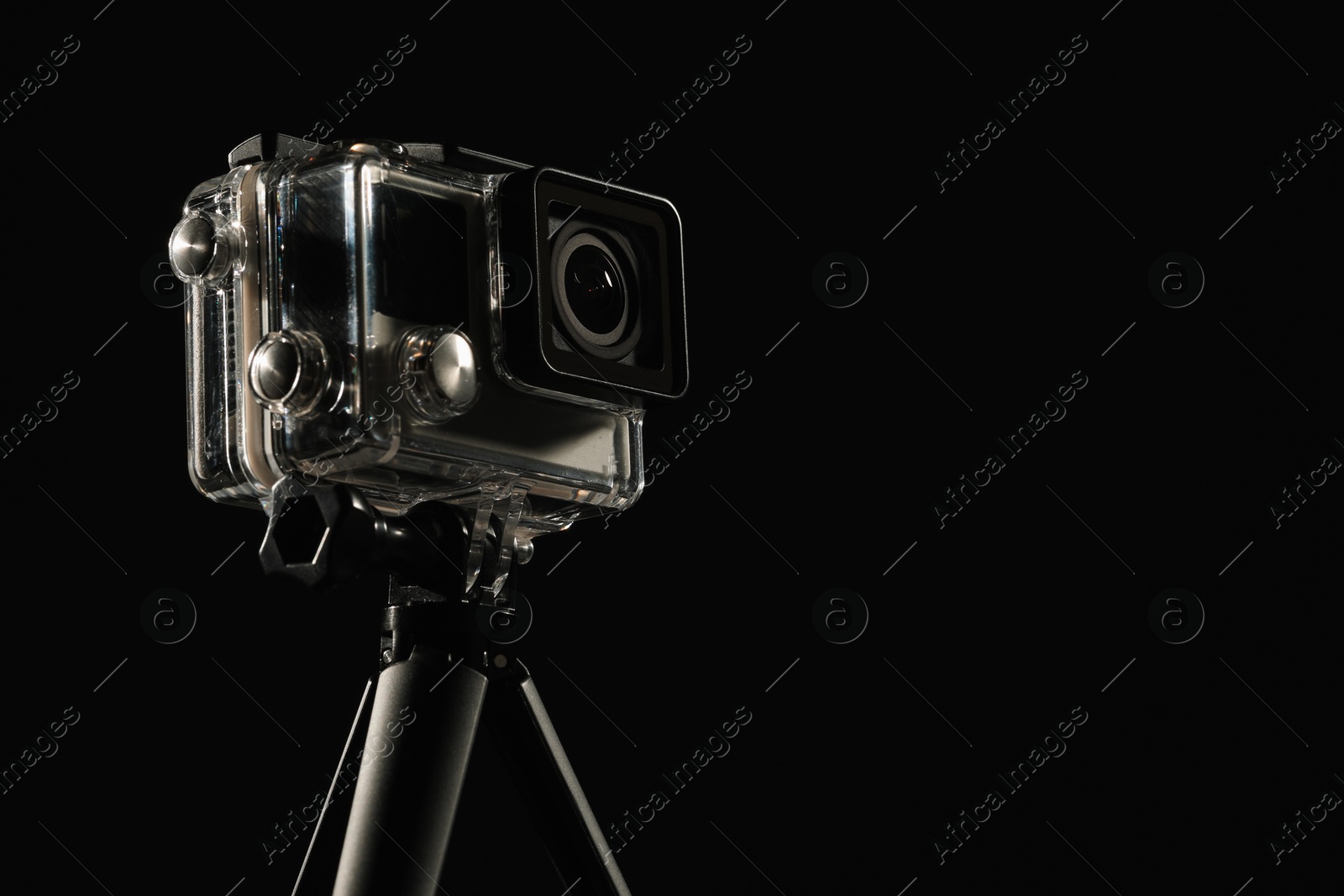 Photo of Modern action camera and tripod against black background, closeup. Space for text