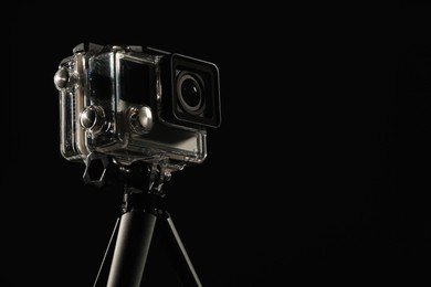 Photo of Modern action camera and tripod against black background, closeup. Space for text