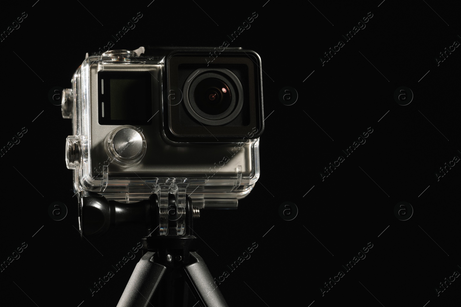 Photo of Modern action camera and tripod against black background, closeup. Space for text