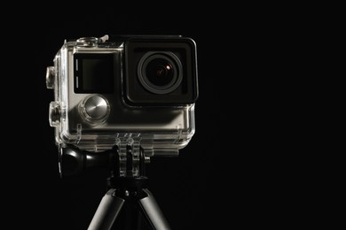 Modern action camera and tripod against black background, closeup. Space for text