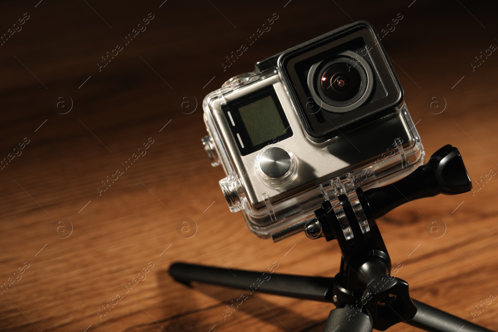 Photo of Modern action camera and tripod on wooden surface, closeup