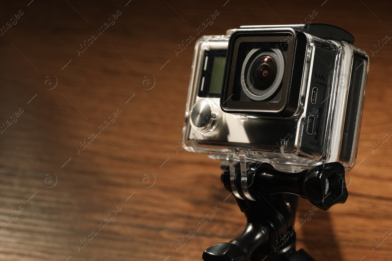 Photo of Modern action camera and tripod on wooden surface, closeup. Space for text