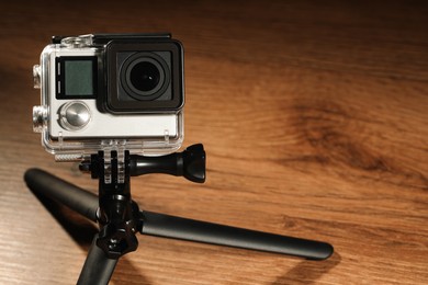 Photo of Modern action camera and tripod on wooden surface. Space for text