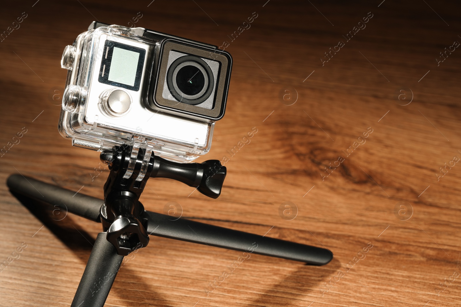 Photo of Modern action camera and tripod on wooden surface. Space for text