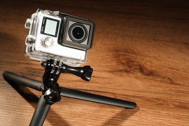 Modern action camera and tripod on wooden surface. Space for text