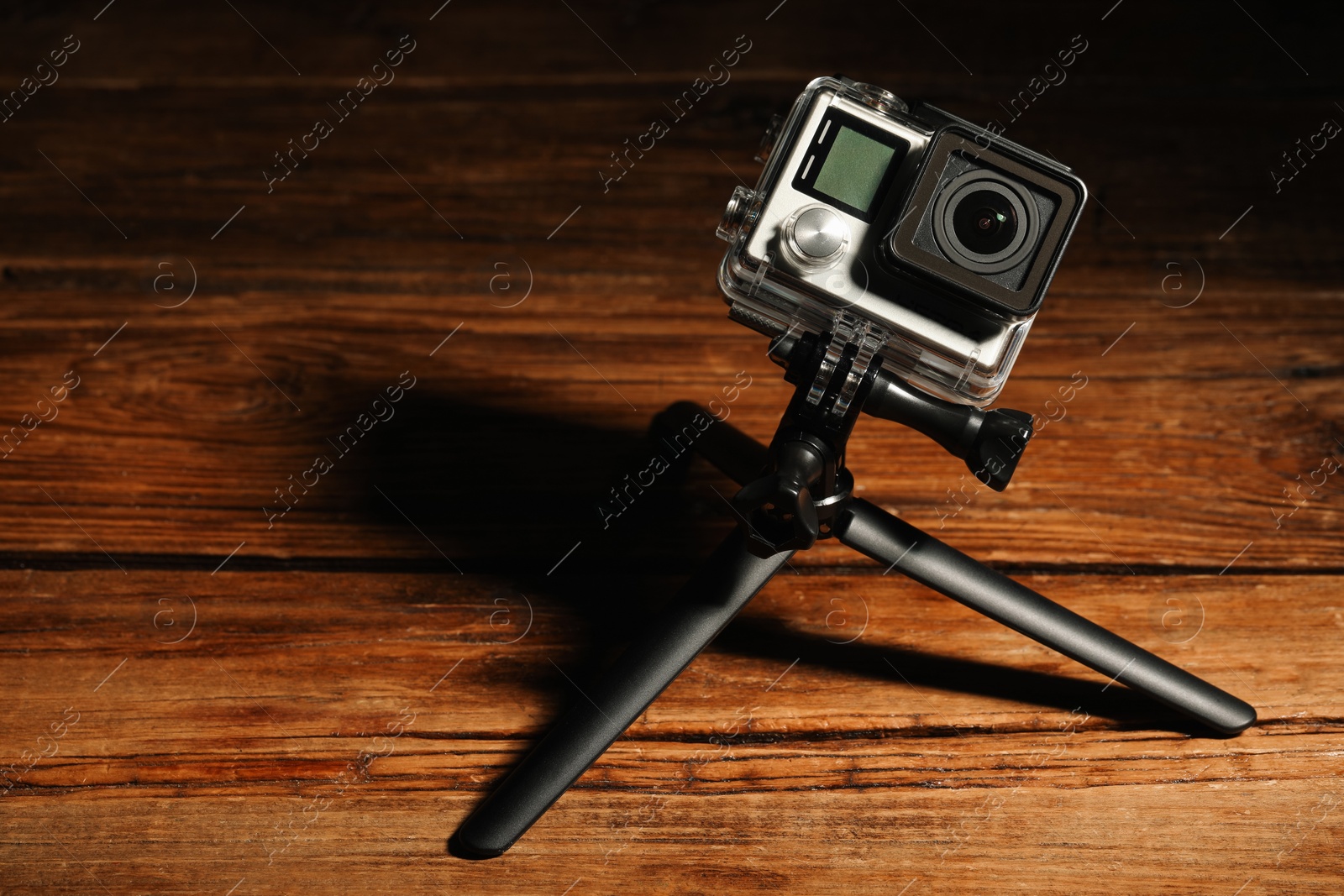 Photo of Modern action camera and tripod on wooden surface. Space for text