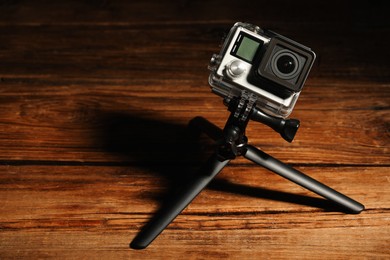 Modern action camera and tripod on wooden surface. Space for text