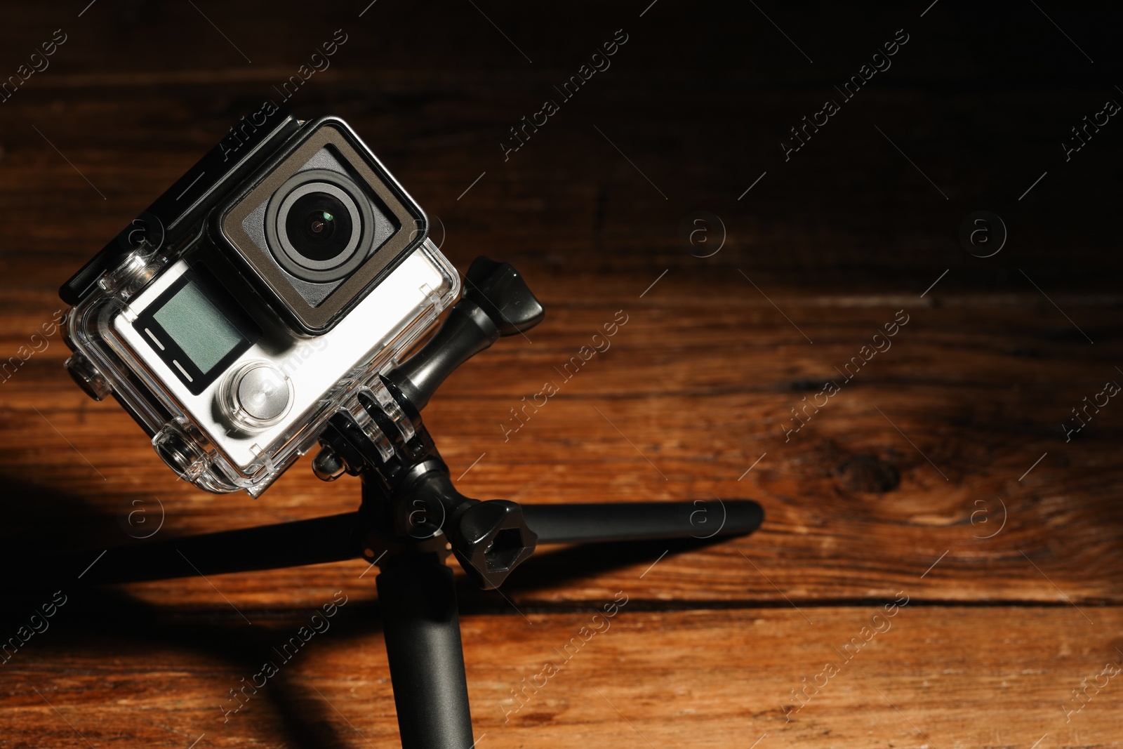 Photo of Modern action camera and tripod on wooden surface. Space for text