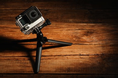 Modern action camera and tripod on wooden surface. Space for text