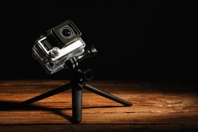 Modern action camera and tripod on wooden surface against black background. Space for text