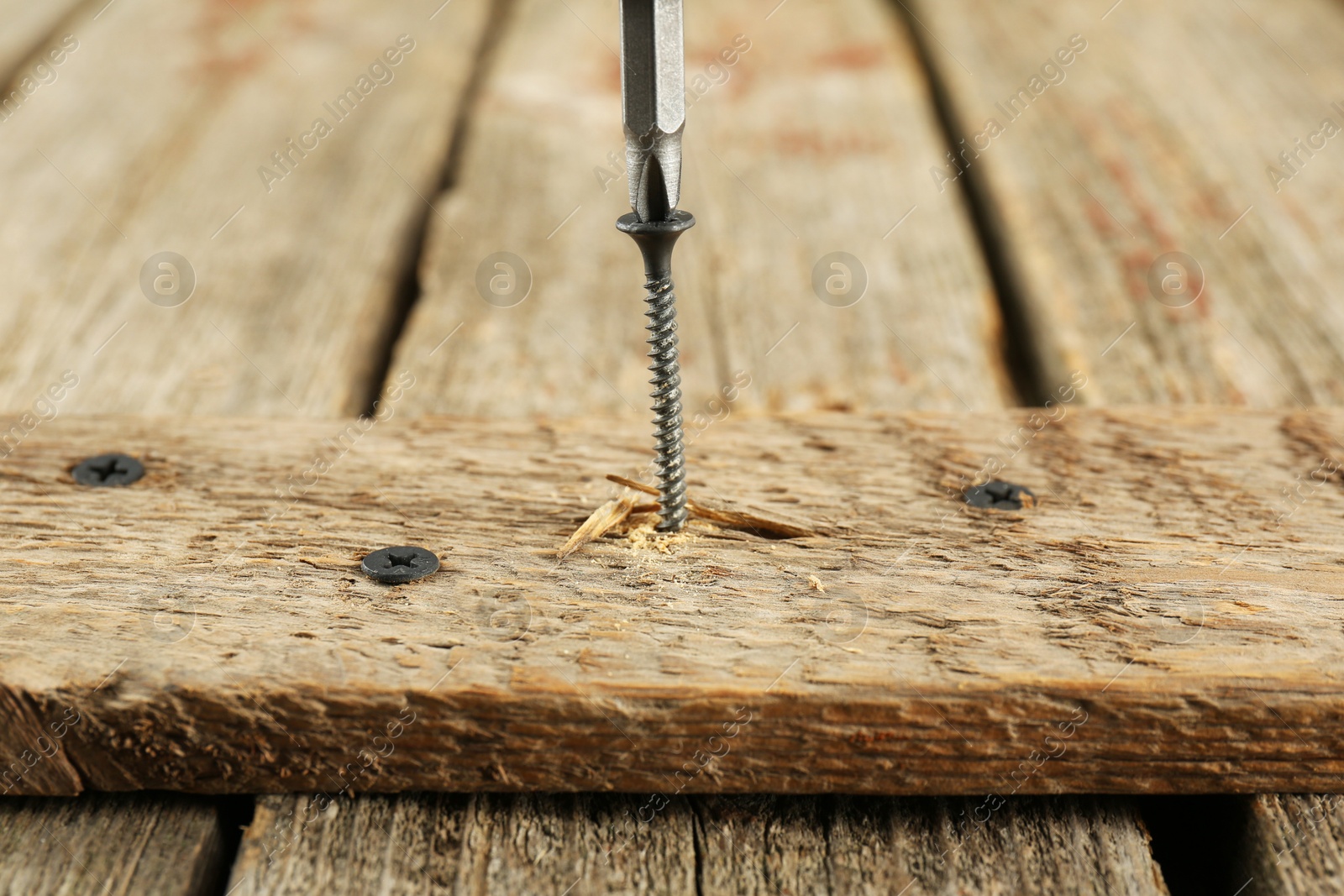 Photo of Screwing screw into wooden plank on table, closeup