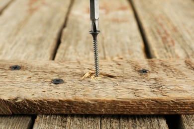 Screwing screw into wooden plank on table, closeup