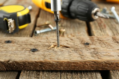 Photo of Screwing screw into wooden plank on table, closeup