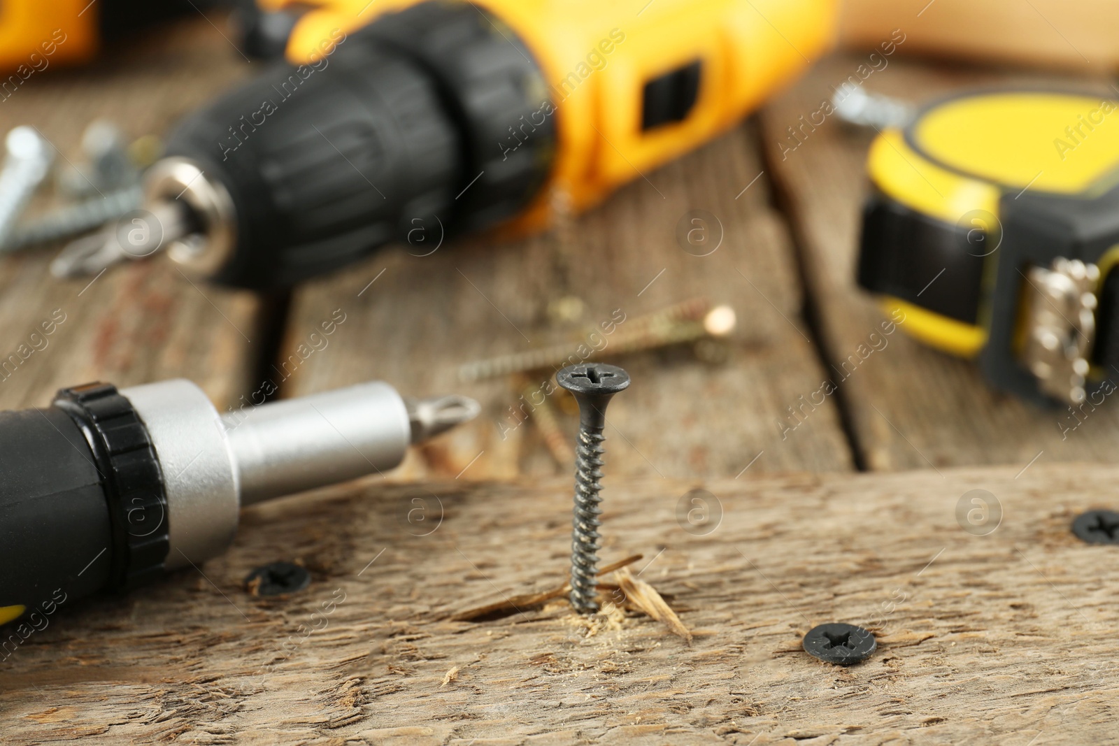 Photo of Screw in wooden plank and equipment on table, closeup