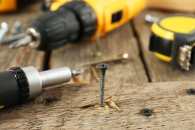 Screw in wooden plank and equipment on table, closeup