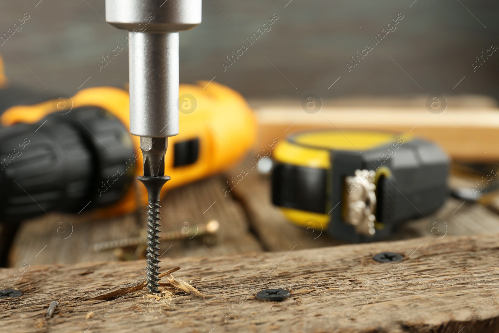 Photo of Screwing screw into wooden plank on table, closeup