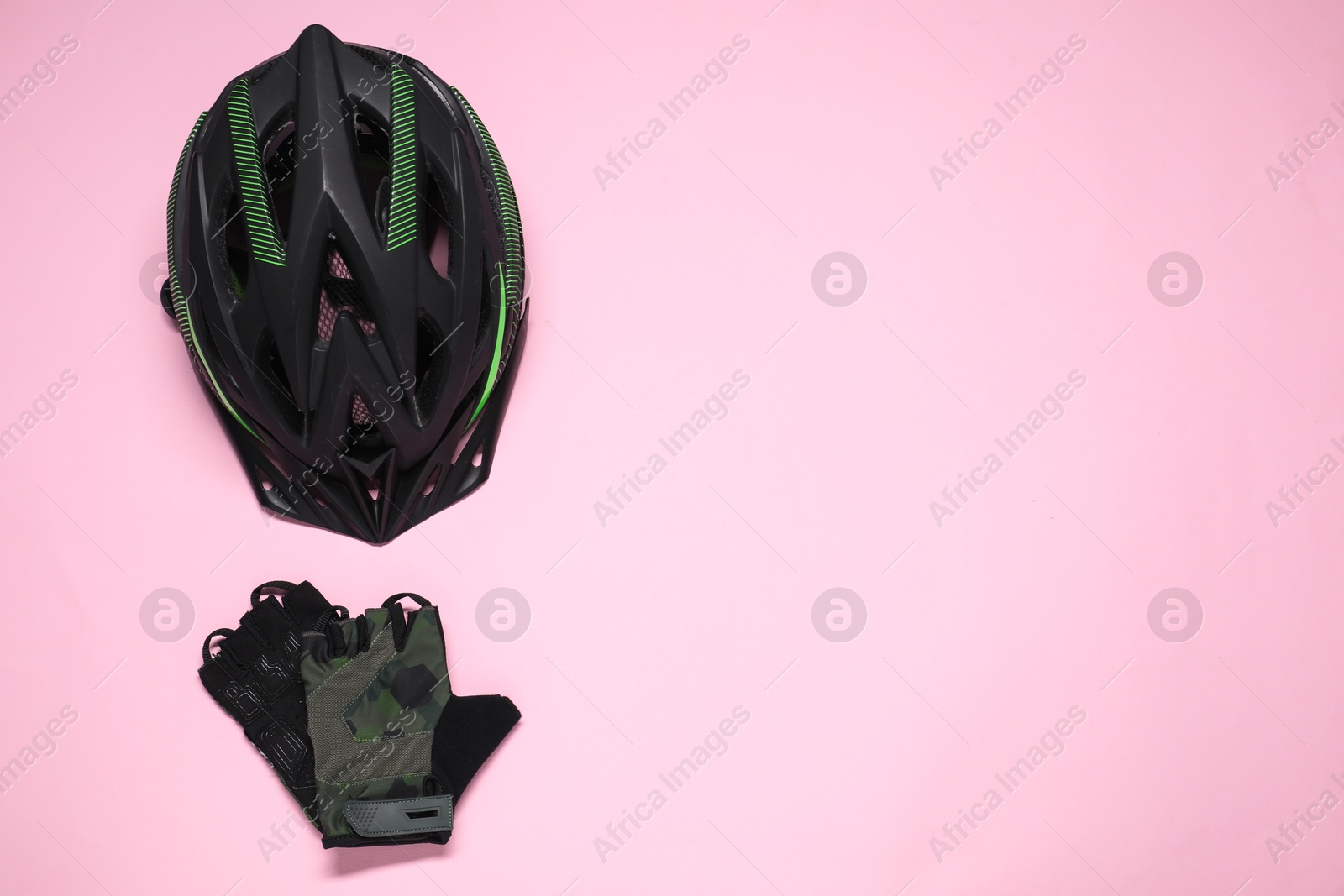 Photo of Bicycle helmet and fingerless cycling gloves on pink background, flat lay. Space for text