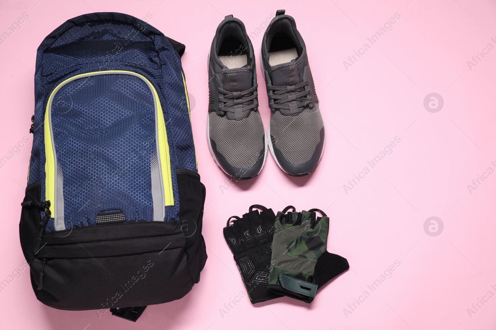 Photo of Backpack, sneakers and fingerless cycling gloves on pink background, flat lay. Space for text