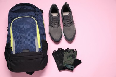 Backpack, sneakers and fingerless cycling gloves on pink background, flat lay. Space for text