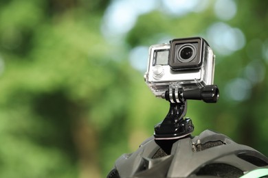 Modern action camera with mount on helmet outdoors, closeup. Space for text