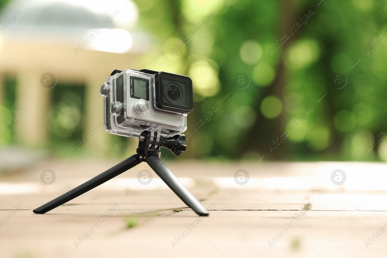 Photo of Modern action camera with tripod on pavement outdoors, space for text