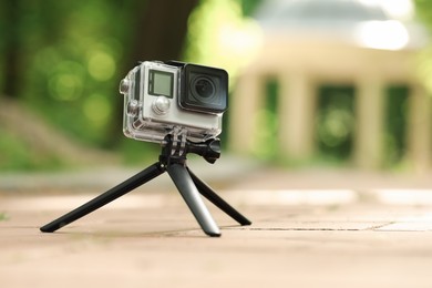 Modern action camera with tripod on pavement outdoors, space for text