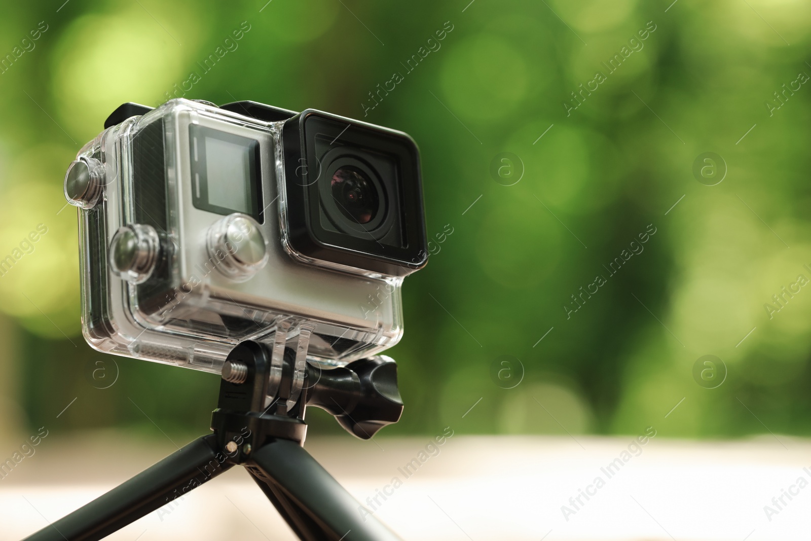 Photo of Modern action camera with tripod outdoors, closeup. Space for text