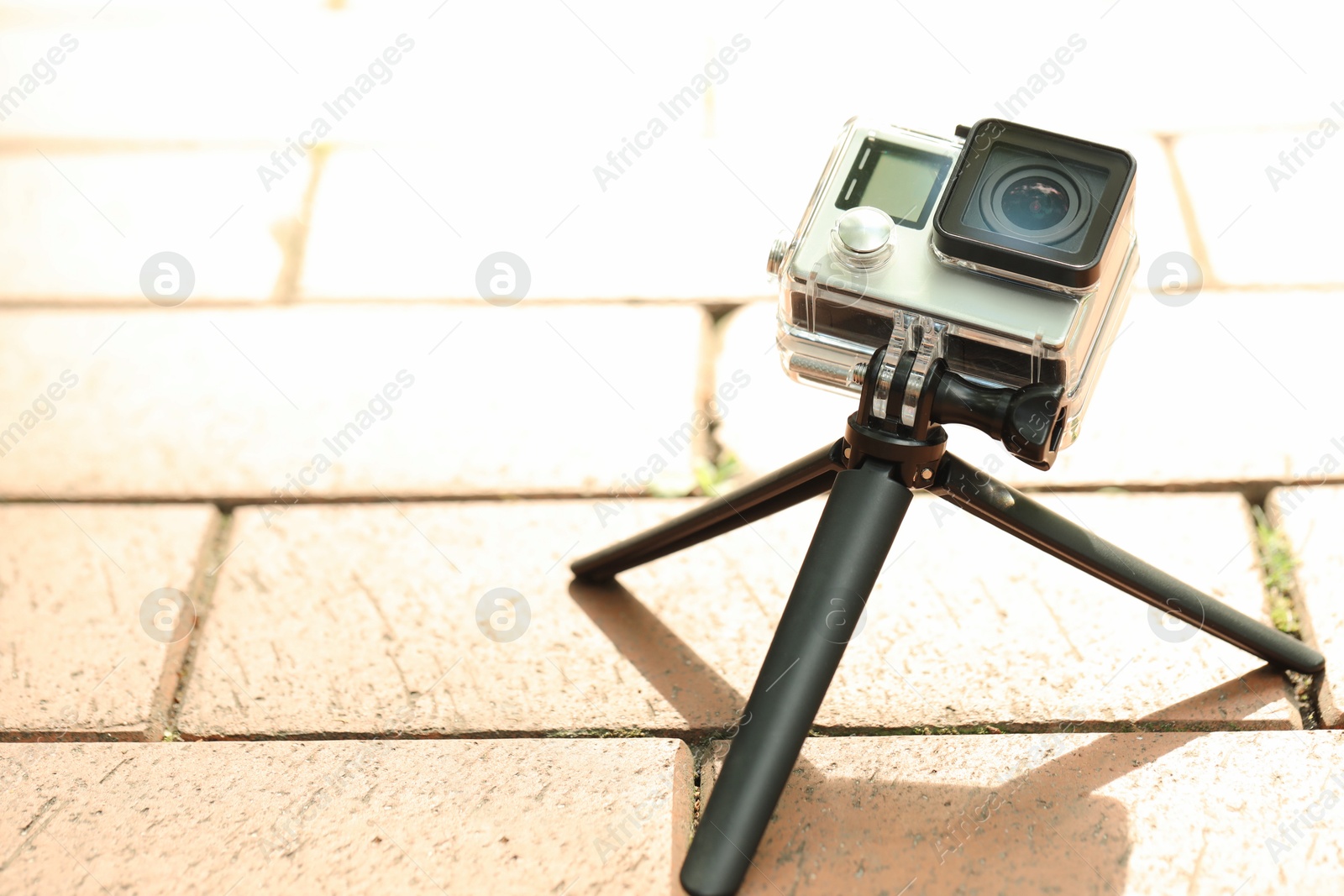 Photo of Modern action camera with tripod on pavement outdoors, space for text